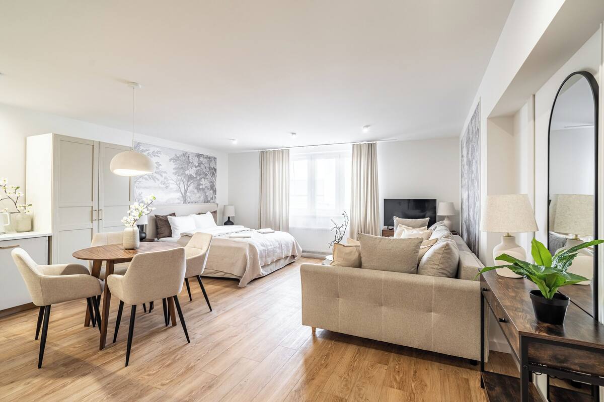 Quarto de hotel moderno com cama, sofá, mesa de jantar, cadeiras e um espelho grande.
