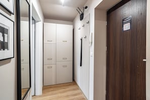 A hallway with a wooden floor, a white wardrobe with multiple drawers, a coat rack, and a door with a QR code. - RentPlanet - Apartamenty Dyrekcyjna (Katowice)