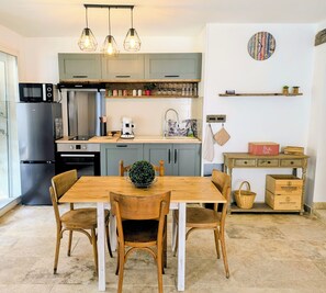 Eine moderne Küche mit Esstisch, Stühlen, einem Kühlschrank, einer Mikrowelle, einer Kaffeemaschine und einer Wanduhr.