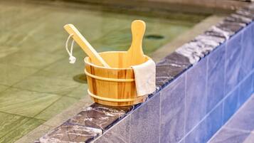 A wooden bucket with a towel and two wooden spoons placed on a tiled pool edge.