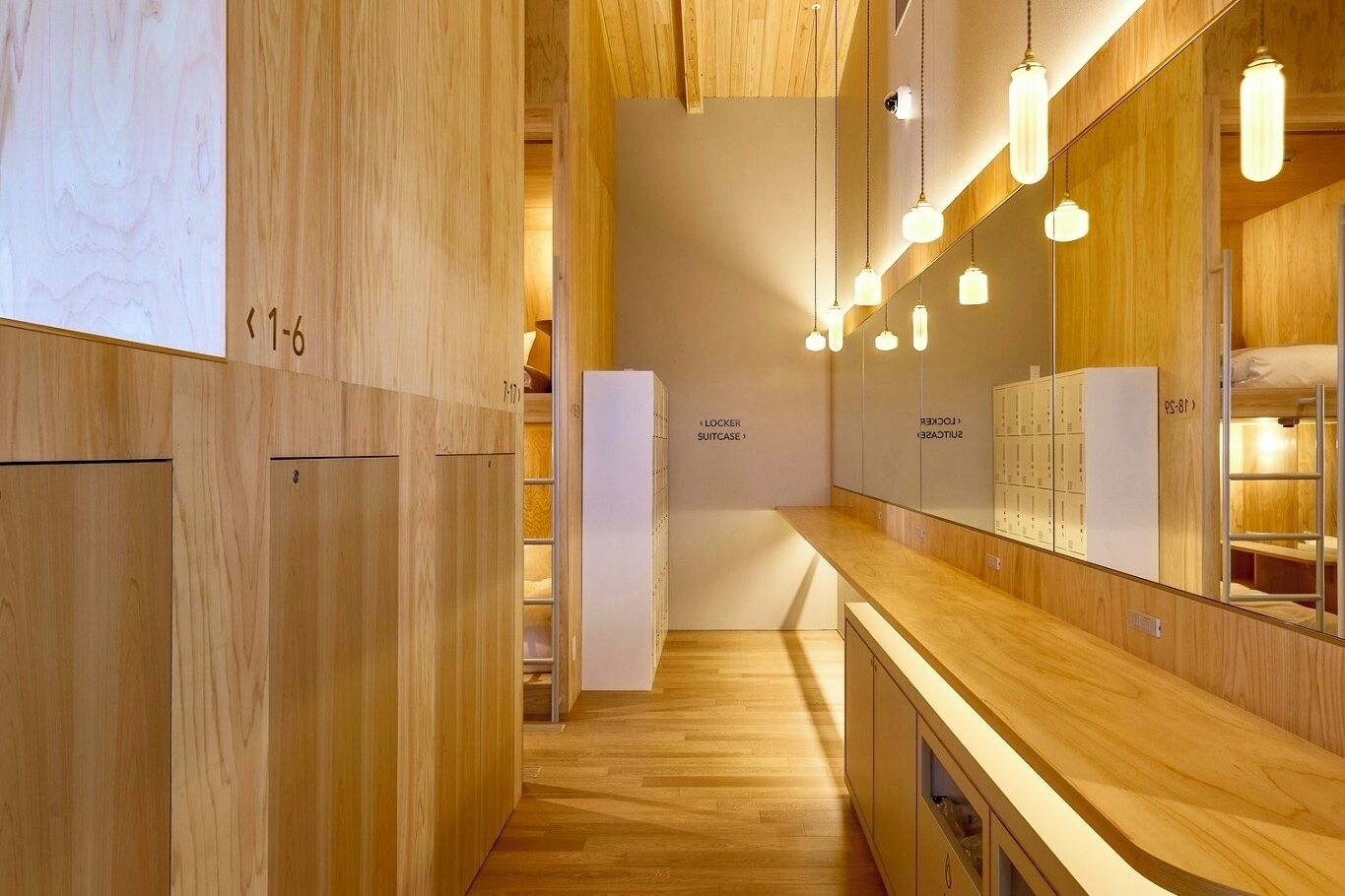 Camera d'albergo moderna con pavimento in legno, una toeletta in legno, uno specchio e un armadio a muro con armadietti numerati.