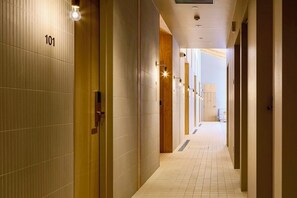 A hotel corridor with numbered doors, a tiled floor, and recessed lighting.