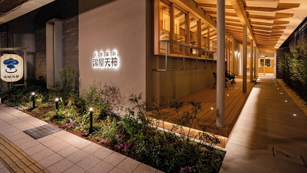 Un edificio con un corredor cubierto, un letrero con caracteres chinos y un jardín con plantas e iluminación.