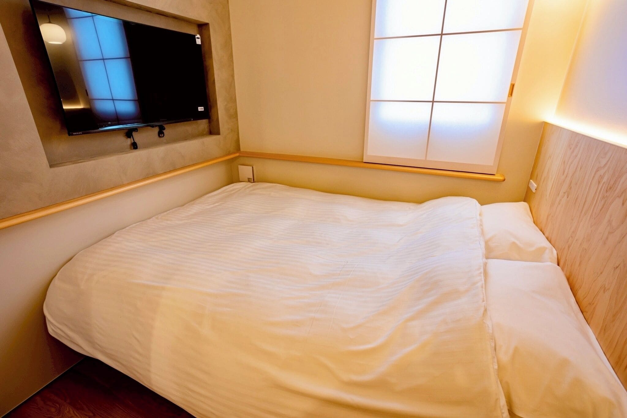 A hotel room with a bed, a television mounted on the wall, and a window with blinds.