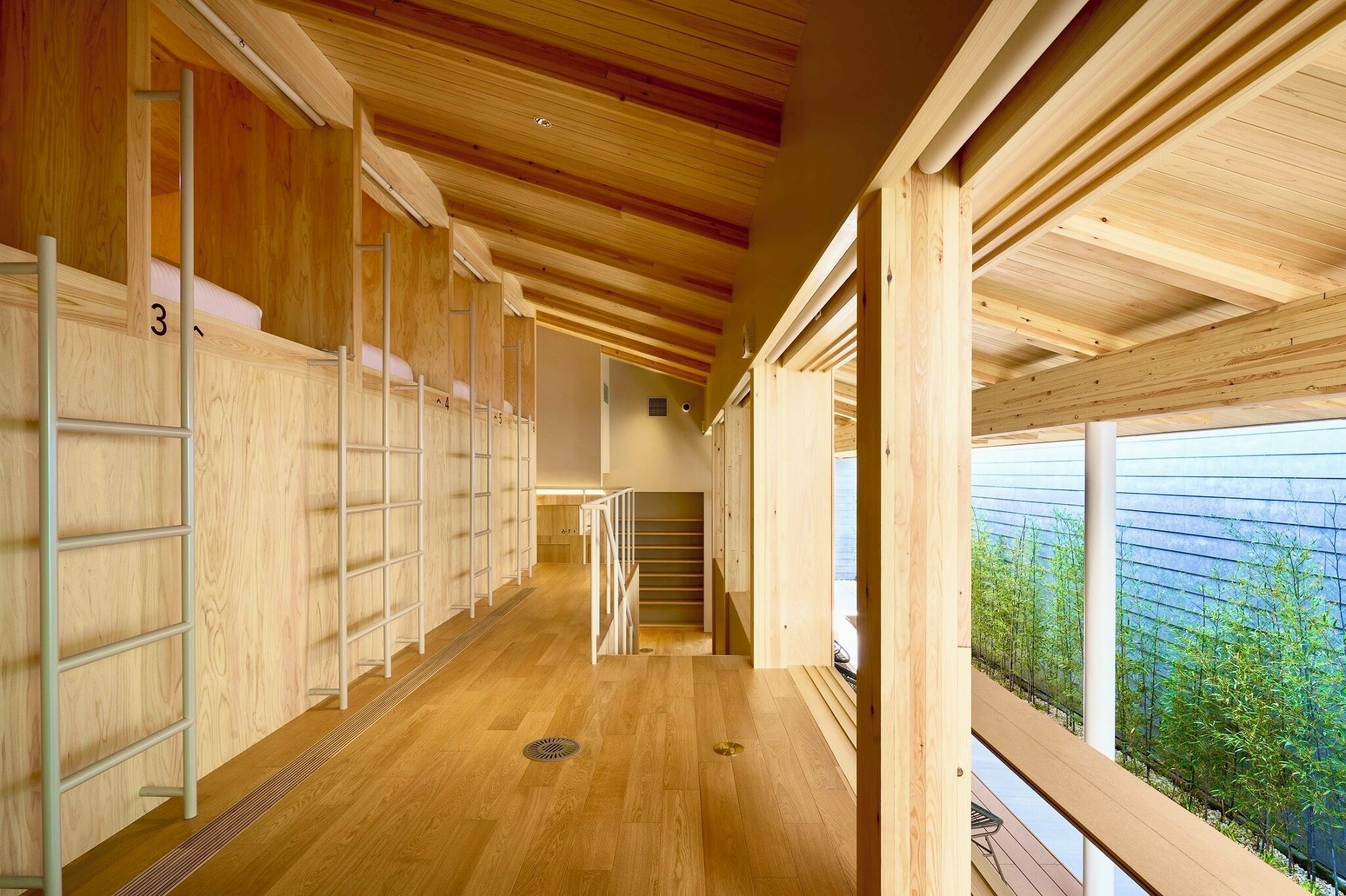 A wooden interior with a central staircase, wooden floors, and a view of greenery outside.