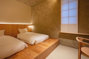 A bedroom with two beds, a wooden headboard, a bedside table, and a window with a view. - Yuya Tenjin - Hostel (Matsue)