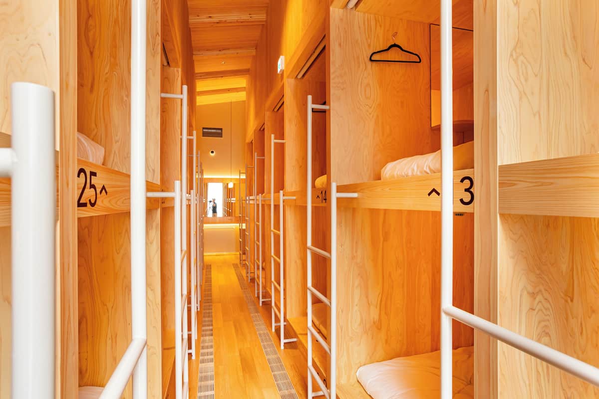 A row of wooden bunk beds with numbers indicating room assignments, a metal ladder, and a wooden floor.