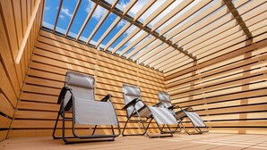Una terraza de madera iluminada por el sol con tres sillones de descanso y un cielo azul despejado.