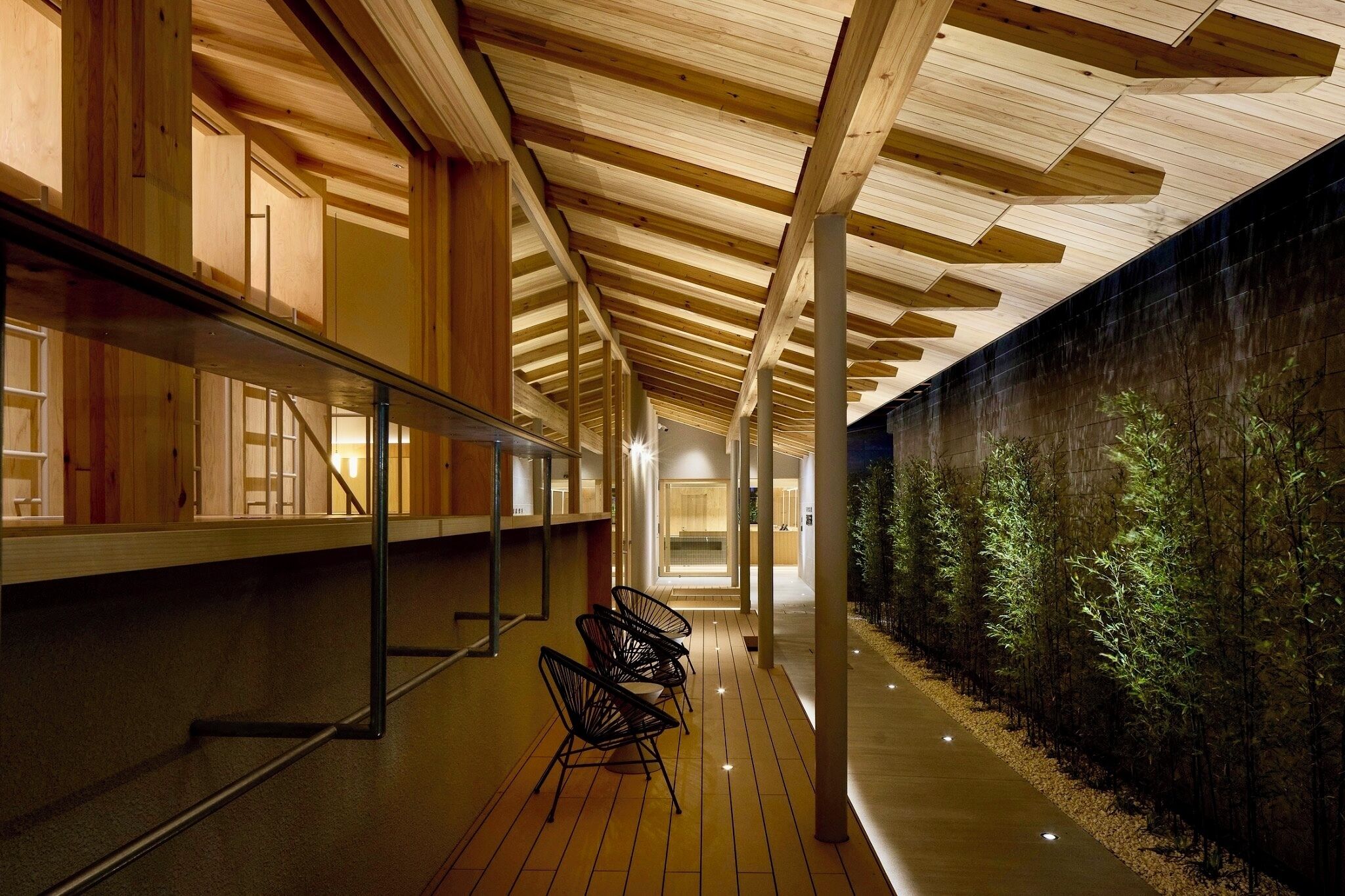 A corridor with wooden beams, a glass wall, and a row of chairs.
