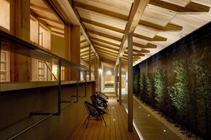 A corridor with wooden beams, a glass wall, and a row of chairs. - Yuya Tenjin - Hostel (Matsue)