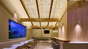 Un restaurante con una barra alargada, sillas de madera y un gran acuario en la pared.