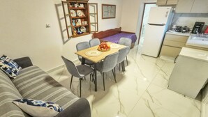 Un espacio habitable compacto con sofá, mesa de comedor, sillas, área de cocina con refrigerador y un mueble decorativo con vajilla.