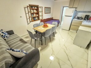 A compact living space with a sofa, dining table, chairs, a kitchen area with a refrigerator, and a decorative cabinet with dishes. - Aroma Zia_Mint Residence  offers a slower, more authentic way to experience Kos! (Lagoudi Zia)
