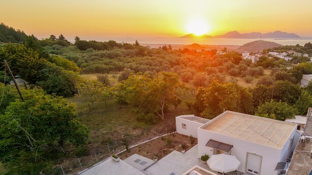 Un barrio residencial con una casa de techo plano, un pequeño patio con sombrilla y vistas al atardecer sobre un paisaje montañoso.