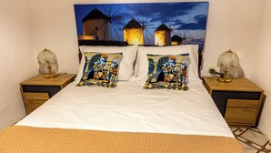 Una cama con sábanas blancas, dos almohadas decorativas, un plaid color beige y dos mesitas de noche con lámparas.