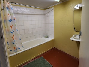 A bathroom with a bathtub, a sink, a mirror, and a shower curtain with a foot pattern. - Hotel Cecil Wondai (Wondai)