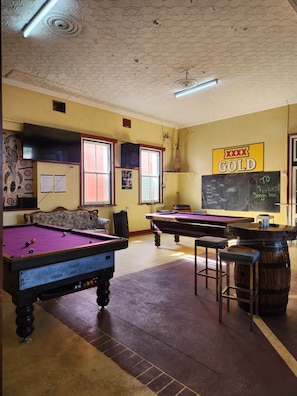 Una sala de billar con dos mesas de pool, un bar y un cartel que indica 'XXX GOLD'.
