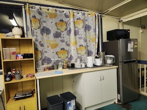 A compact kitchen with a microwave, toaster, and refrigerator. There are storage shelves and a trash bin. - Hotel Cecil Wondai (Wondai)