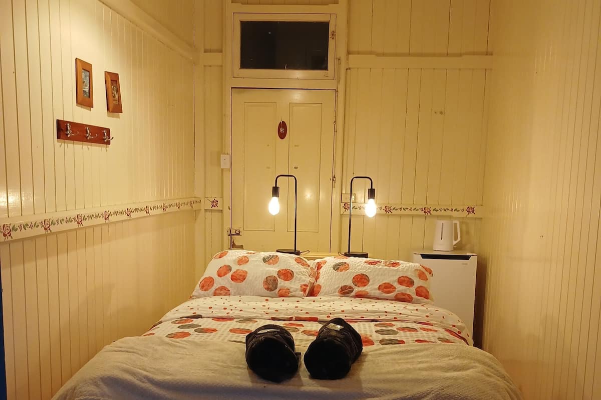 A room with a bed, a window, a door, and a wall-mounted light fixture.