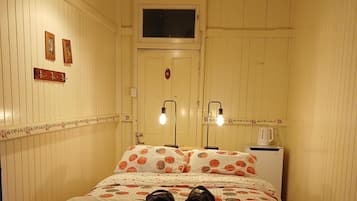Una habitación con cama, ventana, puerta y una lámpara fijada a la pared.