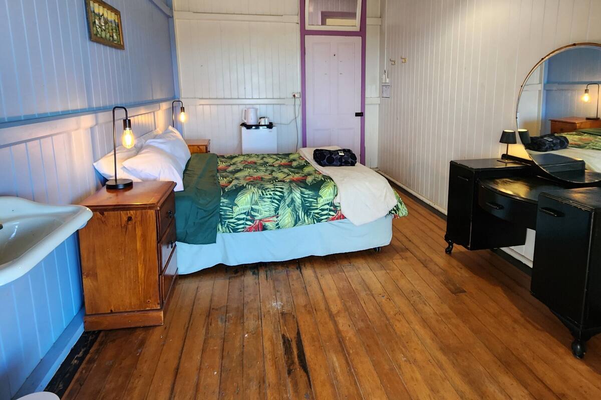 A bedroom with a bed, wooden dresser, bedside table, and a mirror.