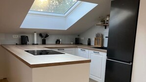 A modern kitchen with a skylight, a black refrigerator, and wooden flooring. - Charming Alpine Apartment with Sauna (Kobarid)