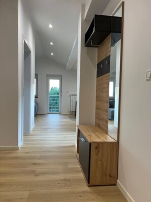 A modern interior with a wooden floor, a built-in bench, and a large mirror. - Charming Alpine Apartment with Sauna (Kobarid)