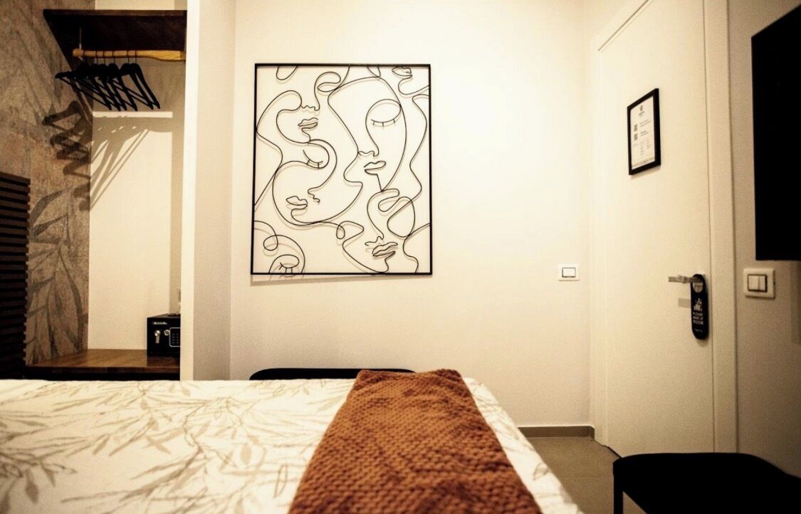 A hotel room with a bed, a wall-mounted artwork, a door, and a bench.