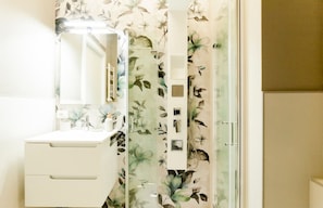 A bathroom with a floral shower curtain, a white sink, and a mirror.