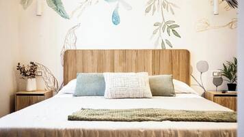Una cama bien hecha con cabecera de madera, dos almohadas, una manta verde y una pared con un mural de temática natural.