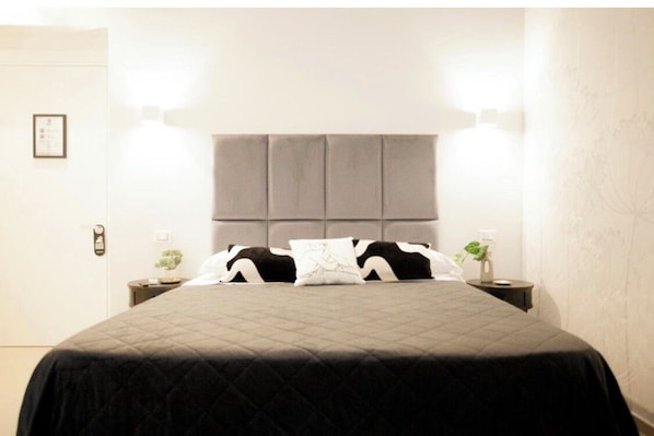 A bed with a quilted bedspread, a grey upholstered headboard, two bedside tables with lamps, and a framed picture on the wall. - Switch holiday 9 (La Spezia)