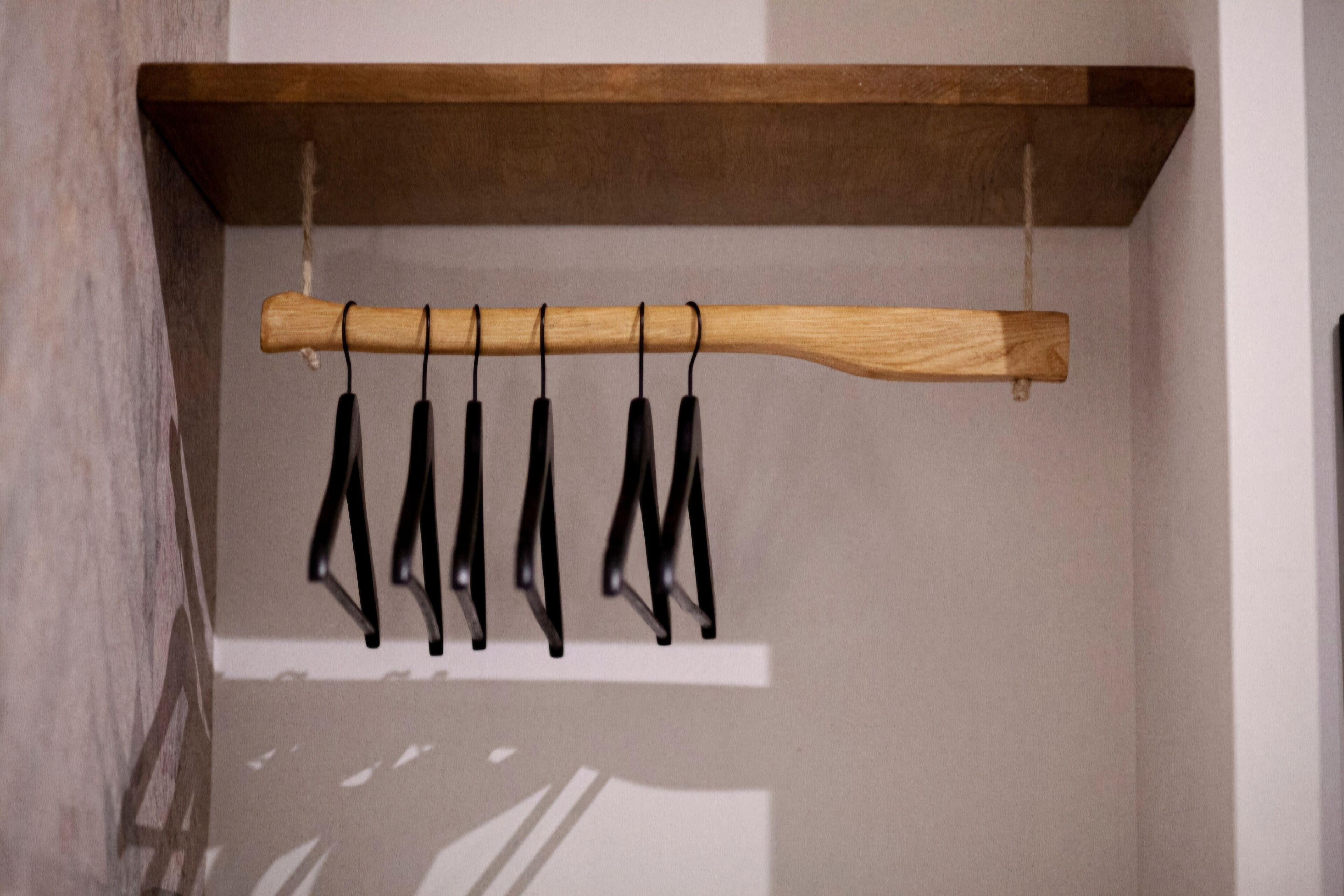 Un perchero de madera con perchas negras junto a una pared.