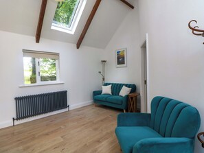 A room with a sloped ceiling, a radiator, a teal sofa, a wooden floor, and a framed picture on the wall.