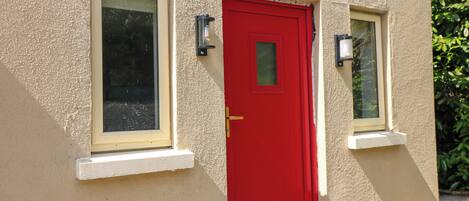 A building with a red door, two windows, and a small outdoor area with a bowl.