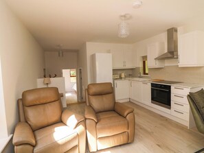 A modern kitchen with white cabinets, a stainless steel range hood, and a black oven. There are two brown leather chairs in a living area with a wooden floor. - THE MEWS @ SUSKAR, pet friendly in Laragh, County Wicklow (Glendalough)