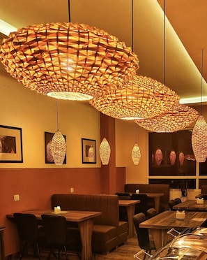 A restaurant interior with multiple hanging pendant lights, cushioned seating, and framed artwork on the walls. - Mandarava Hotel (Gangtok)