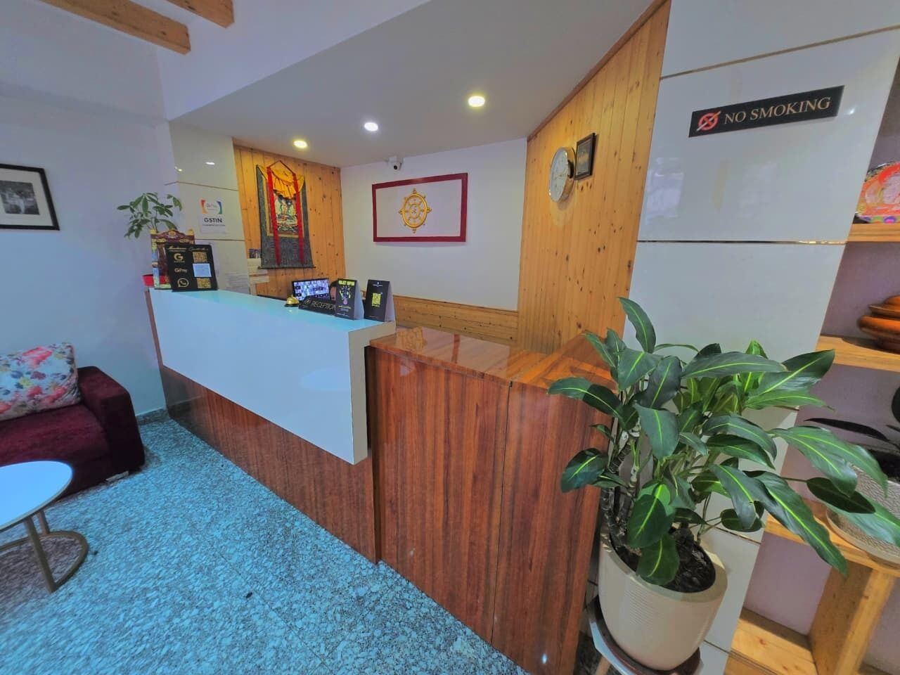 Un área de recepción con un mostrador de madera, un cartel de 'NO FUMAR', un reloj y una brújula enmarcada en la pared.