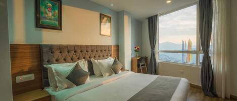 A hotel room with a large bed, a wooden headboard, a desk, and a view of mountains through the window.