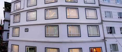 A multi-story building with numerous windows, balconies, and a red awning.