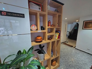 A room with a 'NO SMOKING' sign, a wooden bookshelf, a plant, and a staircase in the background.