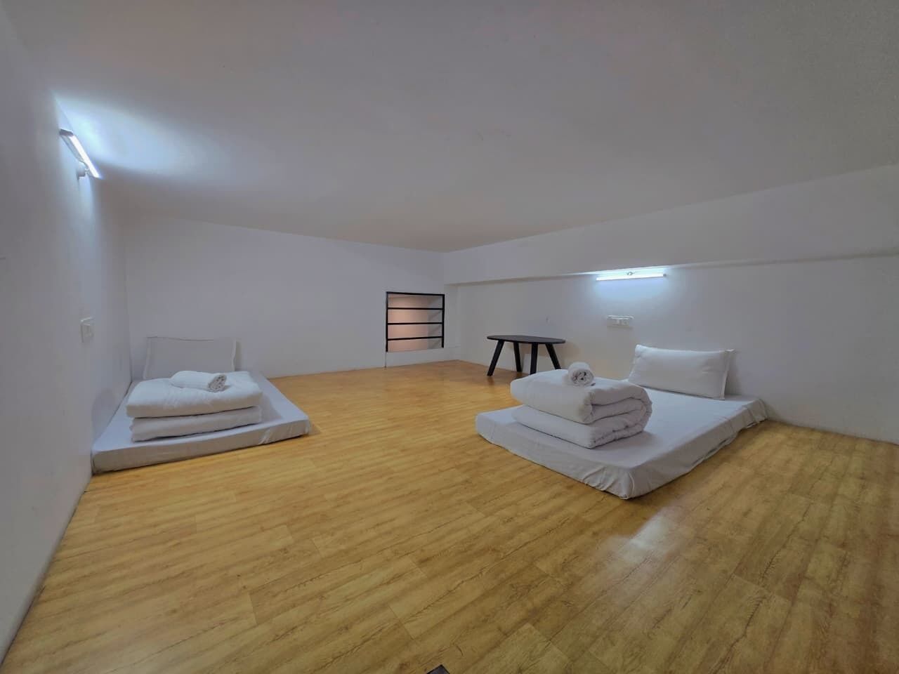 Una habitación con dos camas, una mesita y un estante en la pared.