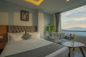 A hotel room with a large bed, a sofa, a small table with flowers, a plant, and a painting on the wall.