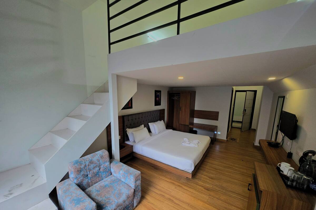 A hotel room with a bed, a sofa, a TV, a desk, and a staircase.