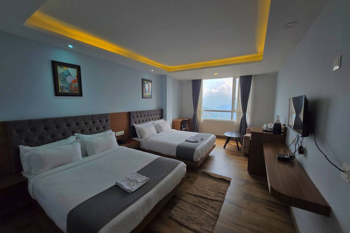 A hotel room with two beds, a desk, a chair, a TV, and a large window with a view.
