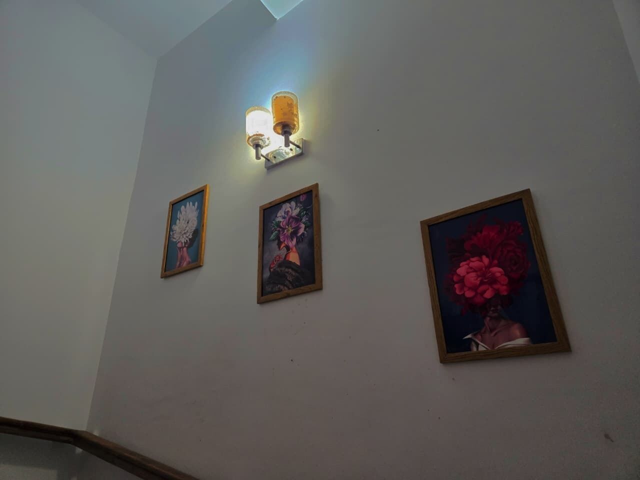 A staircase with three framed floral paintings on the wall and a wall-mounted light fixture.