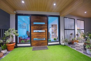 A modern entrance with a glass door, a wooden panel, and a small lawn area.