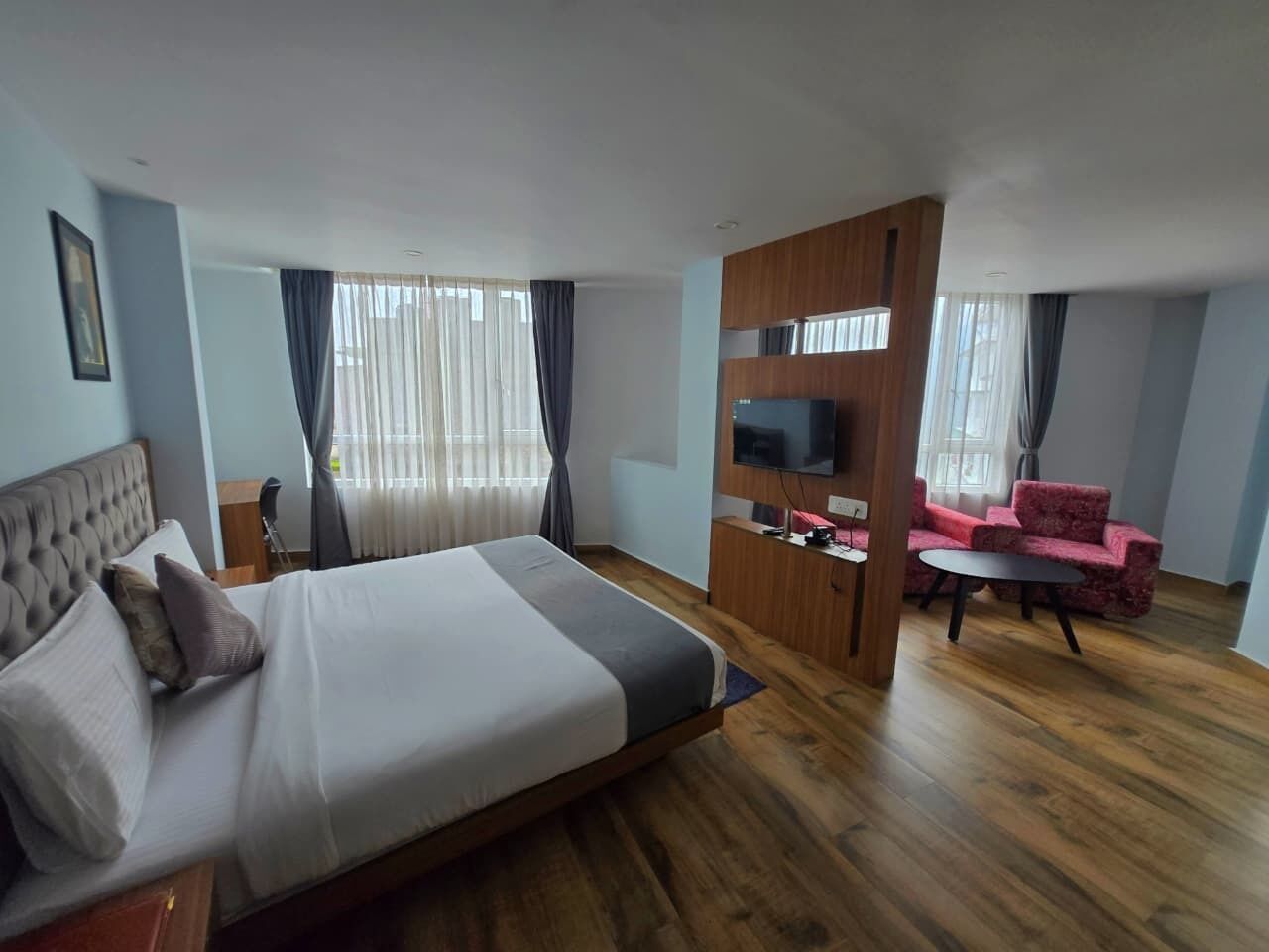 A hotel room with a large bed, a TV, a red sofa, and a wooden partition.