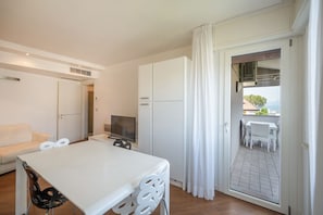 Ein modernes Zimmer mit einem weißen Tisch, Stühlen, einem Fernseher und einem Balkon mit Tisch und Stühlen.