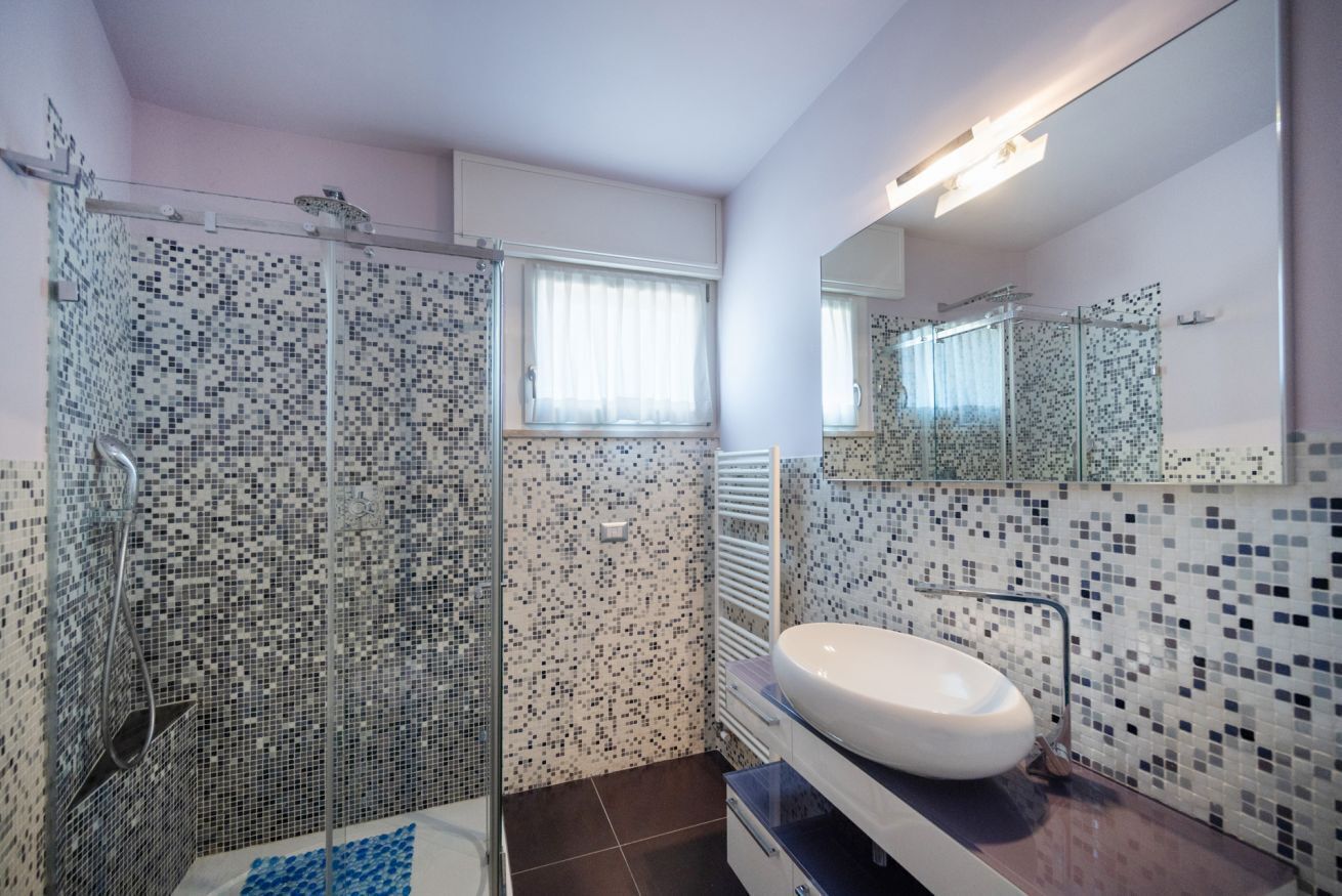 Een badkamer met een douche, wastafel en spiegel.