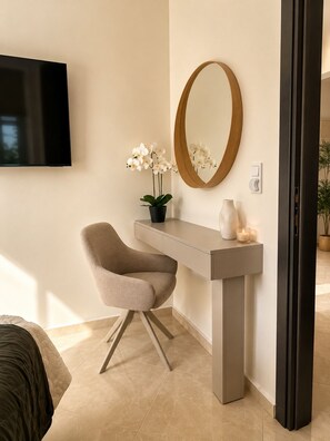 A modern room with a flat-screen TV, a round mirror, a potted orchid, a chair, and a bedside table with a candle. - Luxury Villa with Private Pool & Stunning Cretan Views Near Heraklion (HERAKLION)